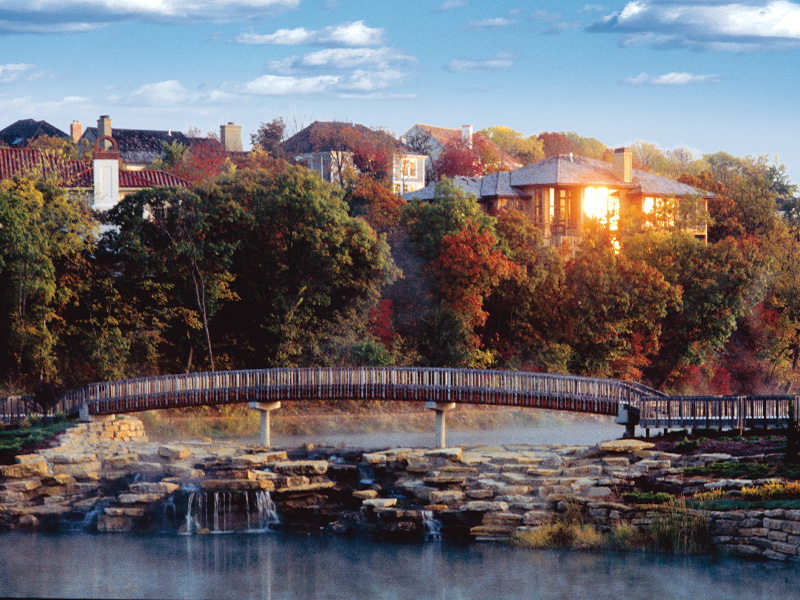 Photo of Pedestrian Bridge and Waterfalls with Homes in the Background at Cedar Creek