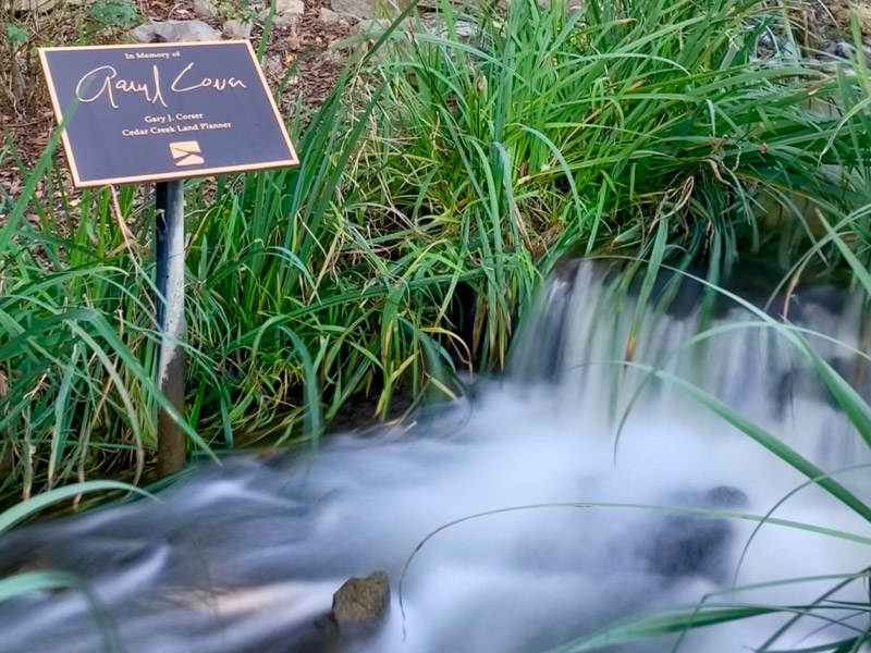 A sign in memory to land planner Gary J Corser next to a Waterfall at Cedar Creek